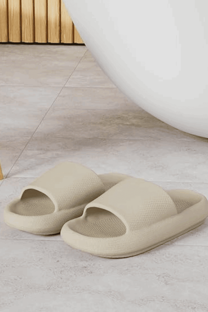 Woman standing in a sunlit room wearing beige BRONAX cloud slides with wide-leg lounge pants – comfy indoor slippers for everyday wear.