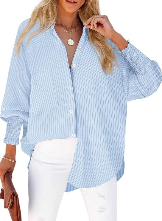 A woman is wearing a blue and white striped oversized button down shirt with white jeans, brown clutch and accessories.