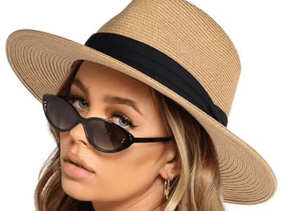 A woman wearing a wide brim straw hat with a black ribbon strip around. She is also wearing sunglasses to complete the look.