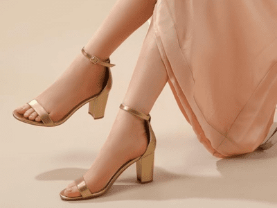 A pair of women's legs in a pretty pink dress, wearing gold heeled sandals.
