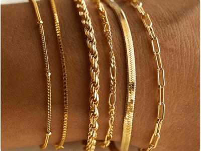 A closeup of a women's wrist wearing six gold bracelets in various designs and sizes.