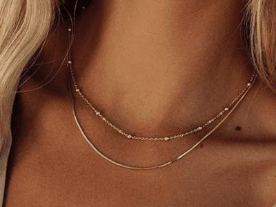 A closeup of a women's neck wearing two dainty gold necklaces.