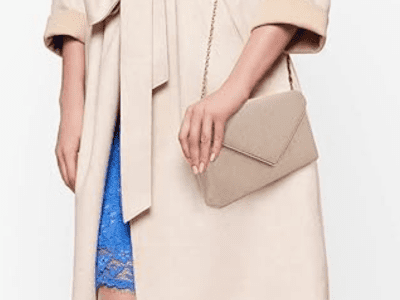 A woman is carrying a nude colored clutch on her shoulder overtop of a nude colored coat.