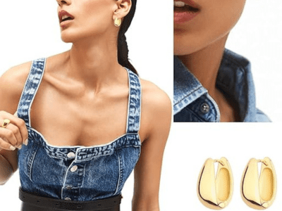A pair of gold chunky earrings being worn by a woman wearing a jean romper.